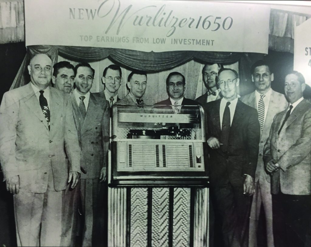 Somewhere back in the ’50s (those “suit-and-tie” days), we find a team of Upstate New York tradesters at the local debut of Wurlitzer’s Model 1650 phonograph, including founding fathers Dick Hilimire (fourth from left in the specs) and his brother Lloyd (fourth from right). Others in this historic photo include Jack Golas, Pat Tarantelli, Tony Zappia, Charlie Wheeler, Al Grant, Jimmy Bilotta and Ed Stanton (who’d originally sold his business to the Hilimire family) at far right. 